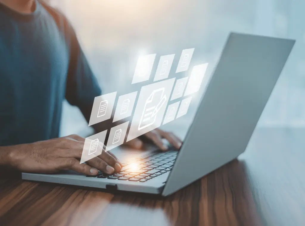 A person types on a laptop with digital file icons floating above the keyboard, symbolizing cloud computing. The scene is modern and tech-focused.